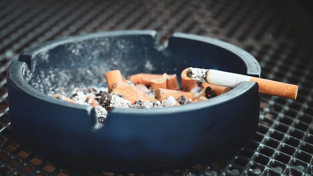Cinzeiro com bitucas e cigarro aceso
