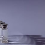 Frascos de vacina enfileirados sobre fundo lilás, projetando sombras