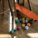 Blocos de madeira coloridos e skate laranja no chão de madeira de uma sala