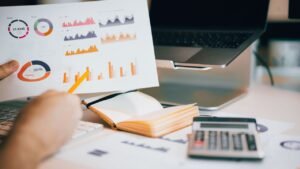 Mãos analisando gráficos impressos ao lado de notebook e calculadora