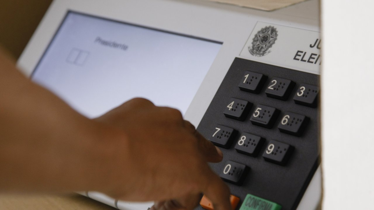 Dedo digitando no teclado de uma urna eletrônica