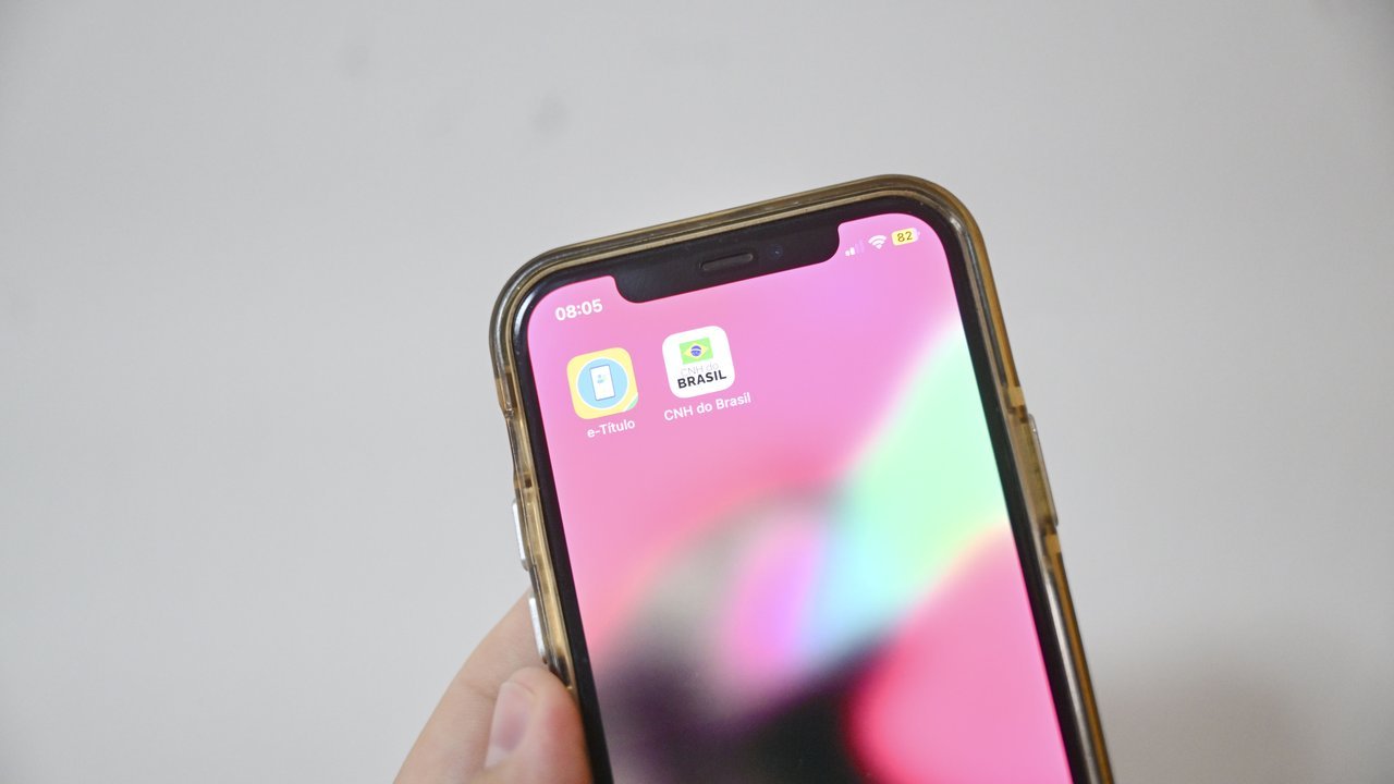 Mão segurando celular com o aplicativo e-Título na tela