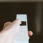 Mão apontando um controle remoto para a televisão