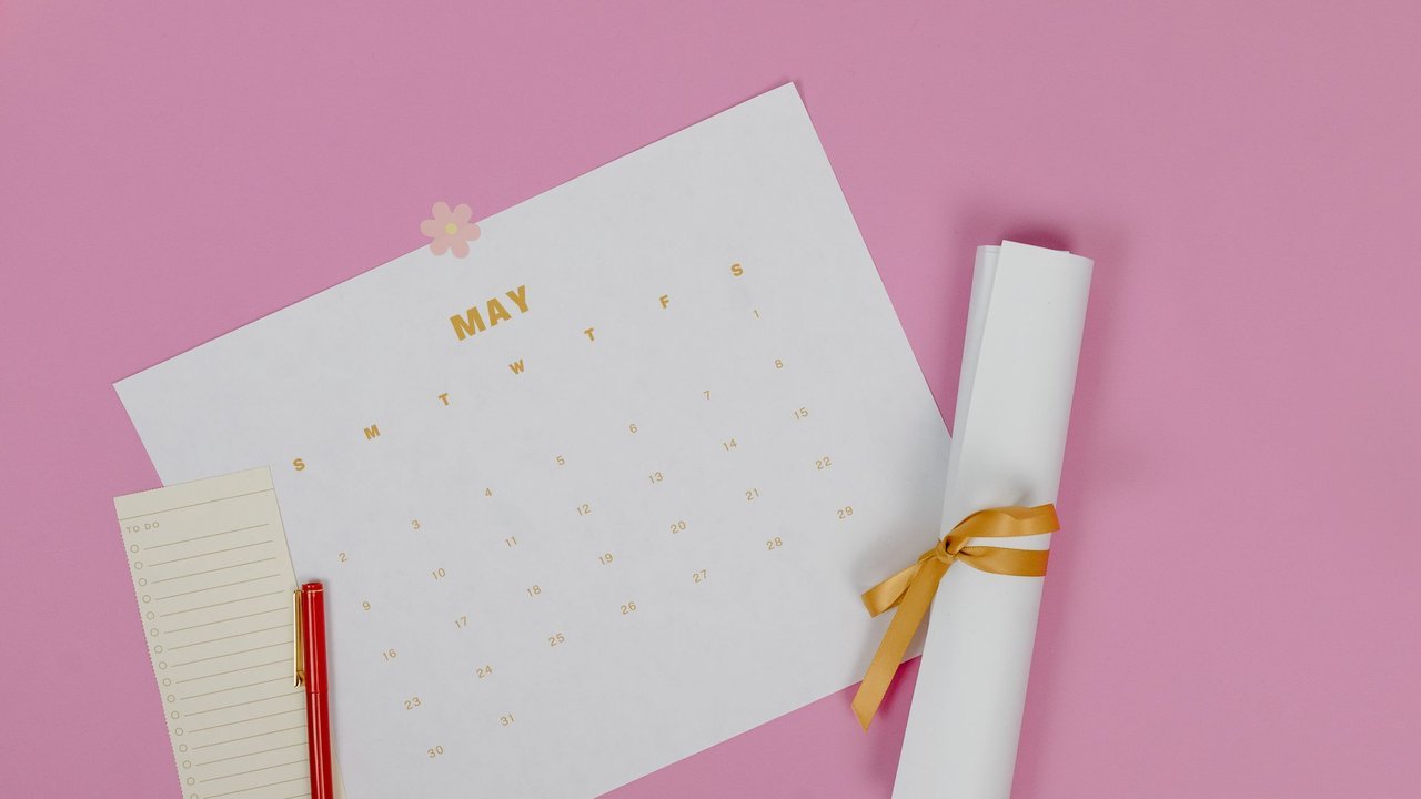 Calendário, lápis vermelho e papel enrolado com laço sobre fundo rosa