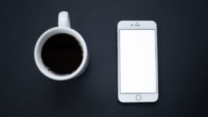 Xícara de café e celular com a tela apagada sobre fundo escuro