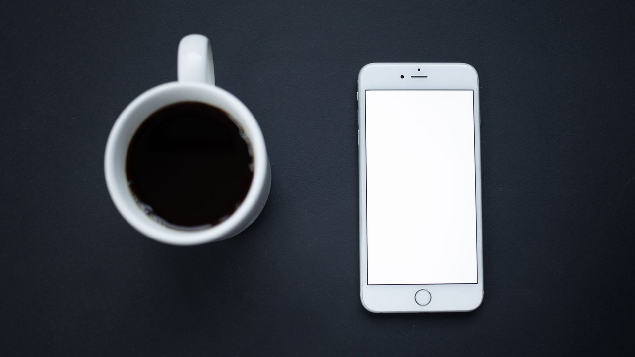 Xícara de café e celular com a tela apagada sobre fundo escuro