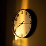 Relógio de parede analógico iluminado por luz quente num ambiente escuro