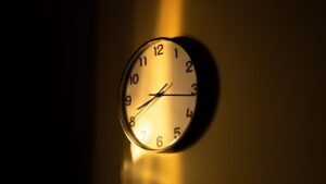 Relógio de parede analógico iluminado por luz quente num ambiente escuro