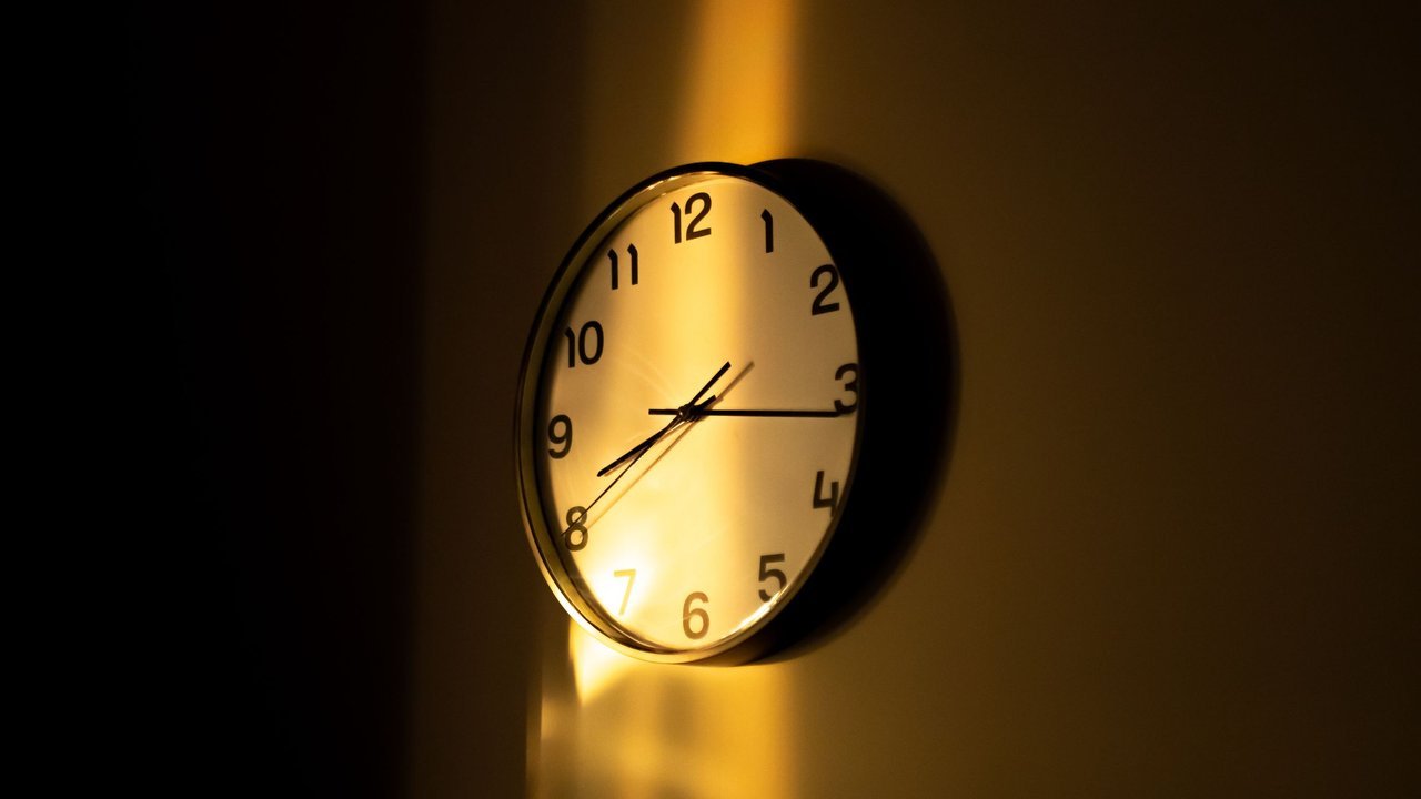 Relógio de parede analógico iluminado por luz quente num ambiente escuro