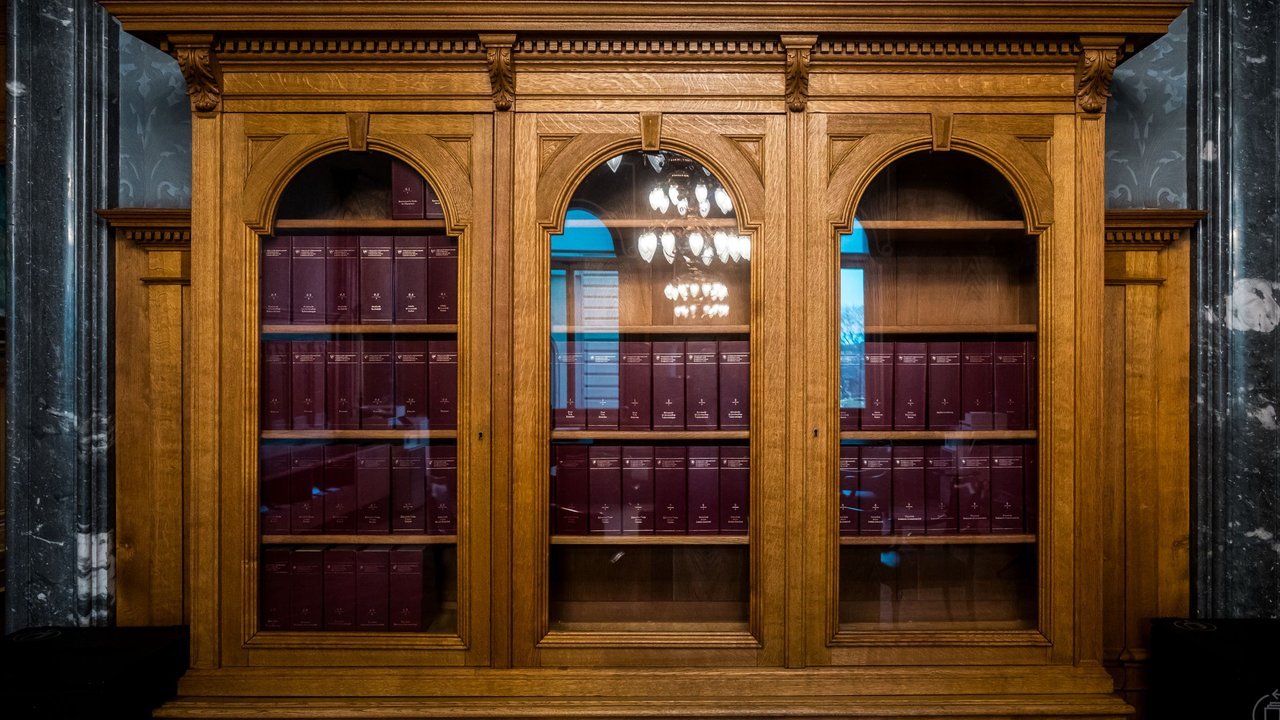 Estante de madeira com livros de capa vermelha numa biblioteca