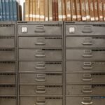 Arquivos de gavetas metálicas sob estantes com livros antigos