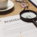 Mesa de trabalho com lupa sobre documentos, xícara de café e cédulas