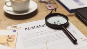 Mesa de trabalho com lupa sobre documentos, xícara de café e cédulas