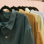 Camisas e casacos em tons de verde, mostarda e rosa pendurados em cabides numa arara