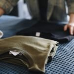 Mãos dobrando roupas infantis sobre uma cama