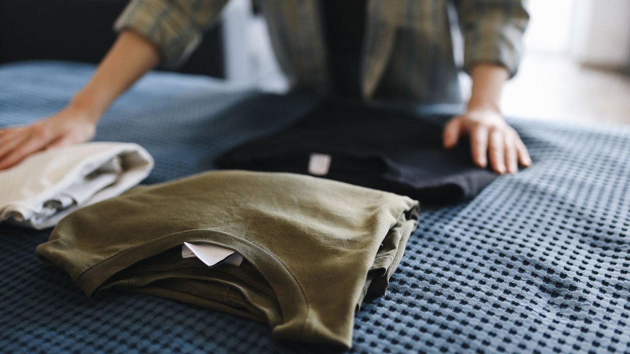 Mãos dobrando roupas infantis sobre uma cama