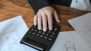 Mão usando calculadora sobre papéis com gráficos e anotações