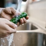 Mãos lavando um pepino sob a água da torneira numa pia de cozinha