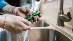 Mãos lavando um pepino sob a água da torneira numa pia de cozinha