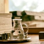 Jarra de vidro com água sobre uma bandeja ao lado de livros, junto à janela
