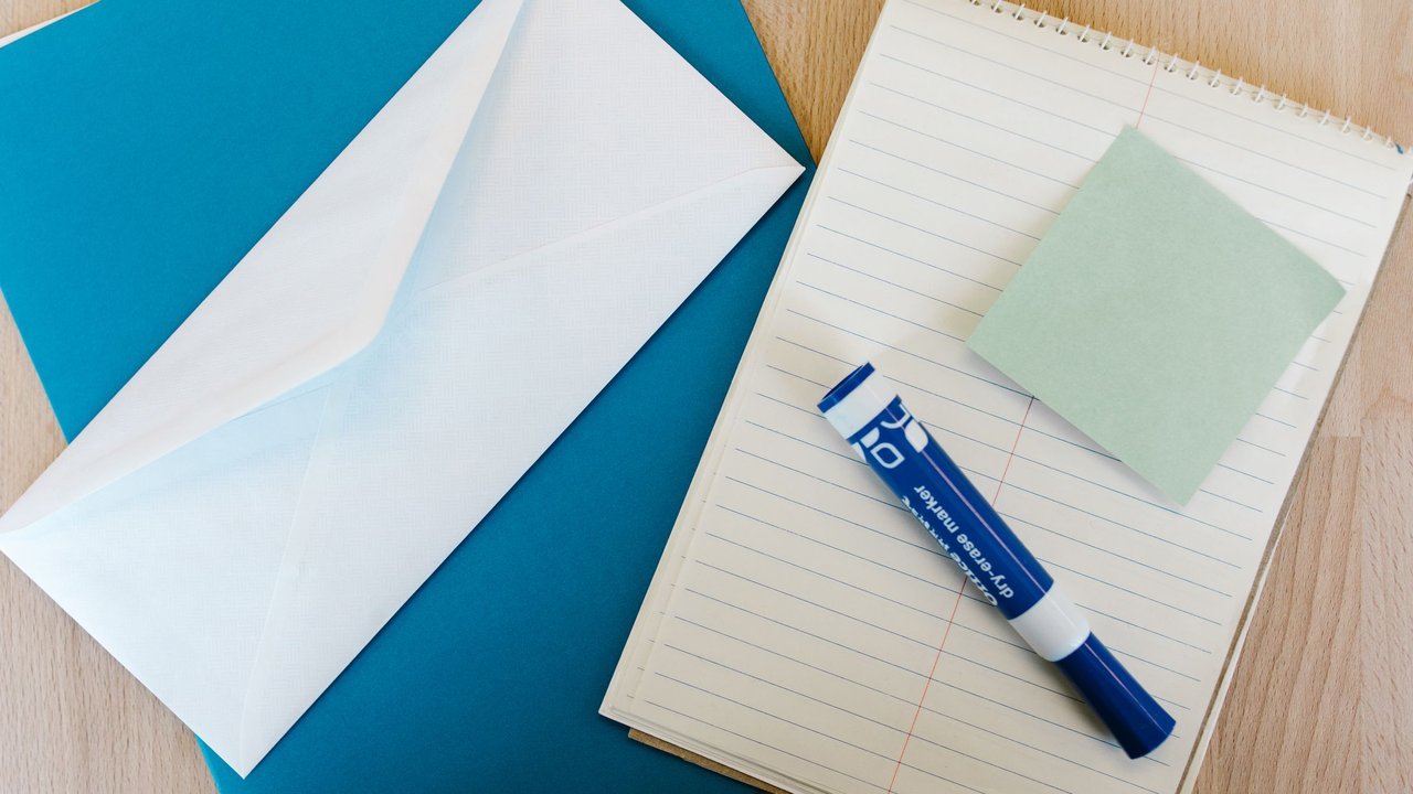 Envelope branco, bloco de notas, post-it e marcador sobre a mesa
