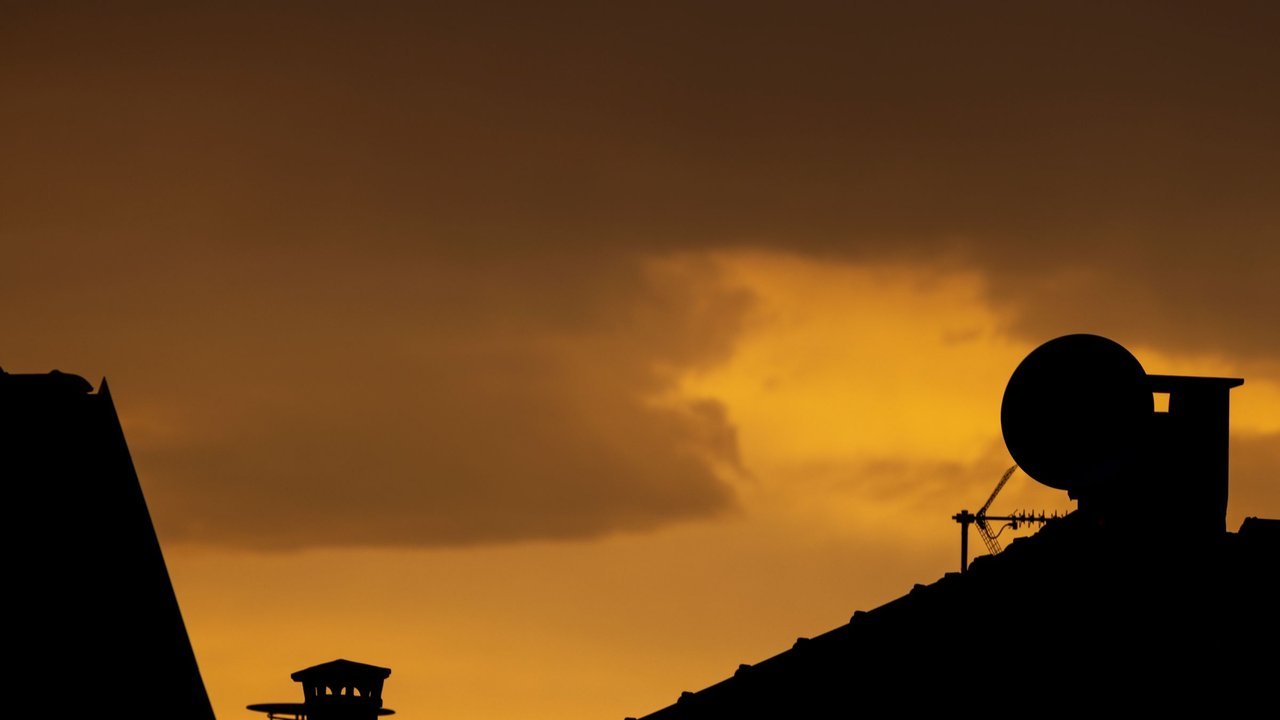 Silhueta de telhado com antena parabólica ao pôr do sol