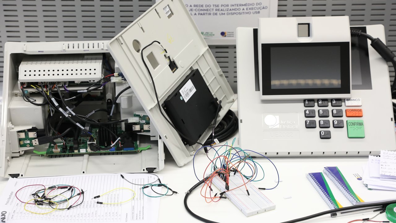 Urna eletrônica aberta com placas e cabos expostos durante teste técnico