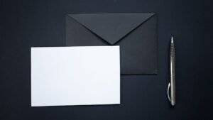 Envelope preto, cartão branco e caneta sobre fundo preto
