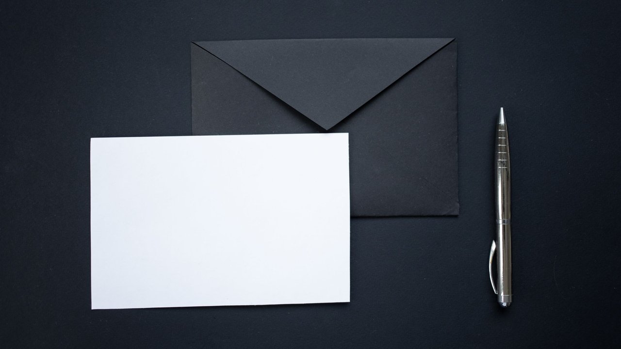 Envelope preto, cartão branco e caneta sobre fundo preto